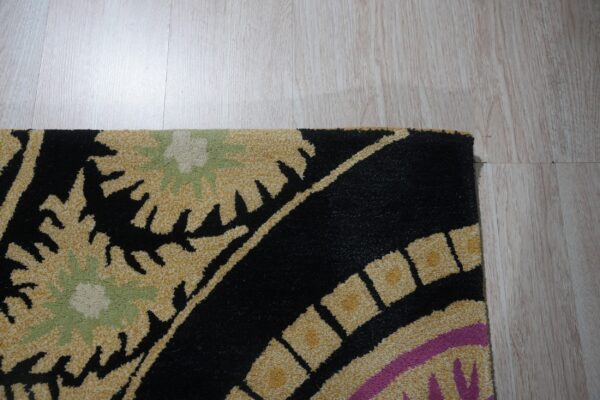 Detail shot of a high-pile rug with black, gold, sage, and magenta patterns on light wood flooring.