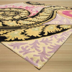 Plush rug with bold black, yellow, pink, and purple paisley patterns rests on light wood planks.