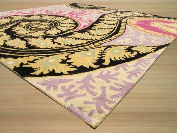 Plush rug with bold black, yellow, pink, and purple paisley patterns rests on light wood planks.