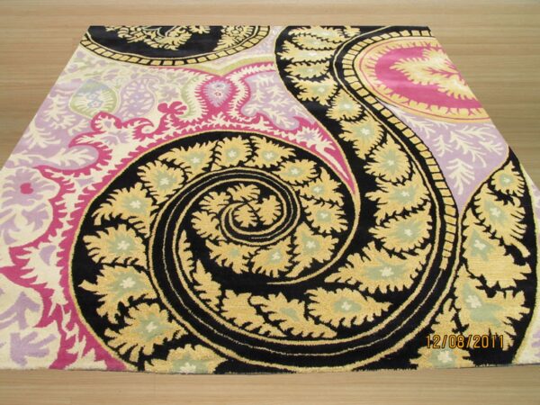Plush rug with a massive swirling paisley pattern in black, gold, bright pink, and lilac on a light wood floor.