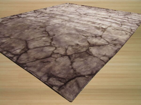 A flat, low-pile brown and gray rug with a cracked stone pattern rests on light wood flooring.