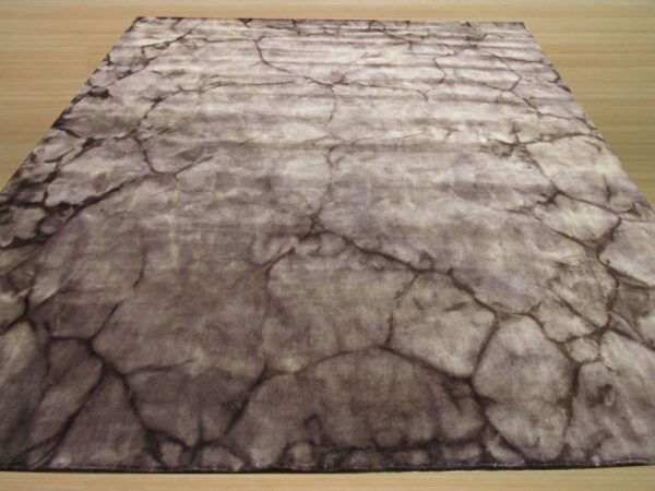 A gray and taupe rug featuring a distressed cracked stone pattern is displayed on light wood flooring.