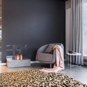 Ornate black and tan rug on gray tile floor next to a swivel chair and a lit fireplace.