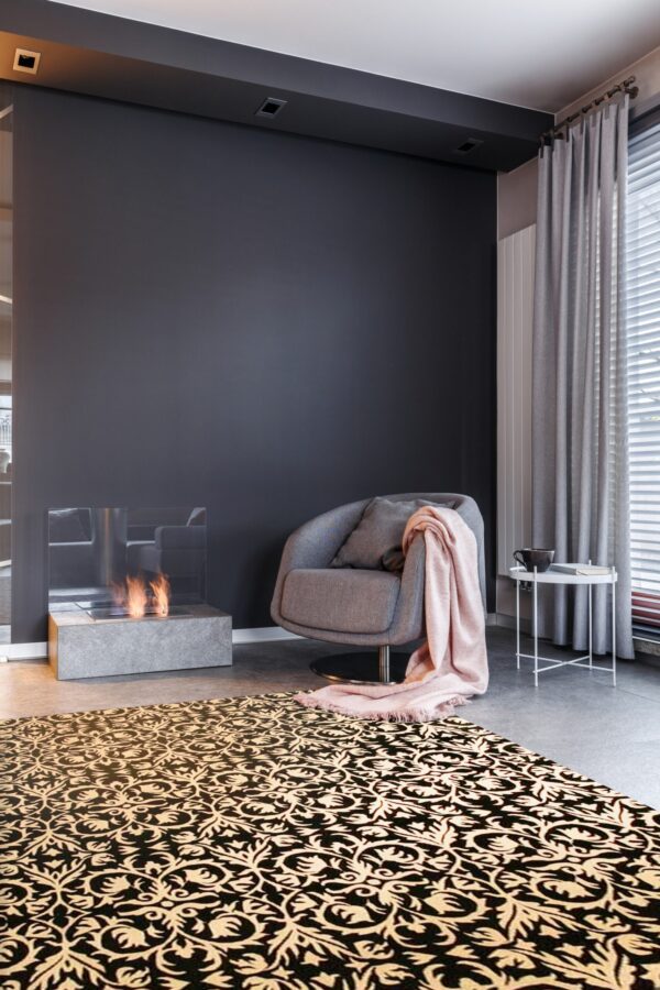 Ornate black and tan rug on gray tile floor next to a swivel chair and a lit fireplace.