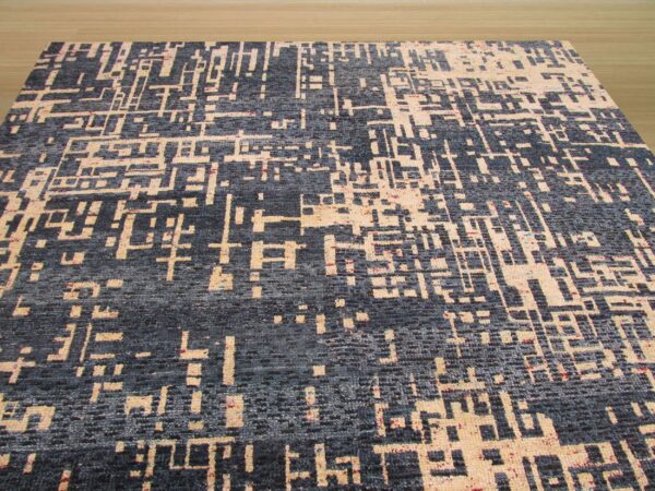 A dark gray rug with an abstract geometric beige pattern rests on light wood floor.