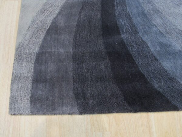 Abstract rug with gray and blue curved color bands displayed on light hardwood planks.