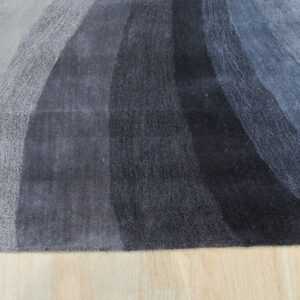 High-pile rug with light to dark gray curved color bands lies on bright wood flooring.