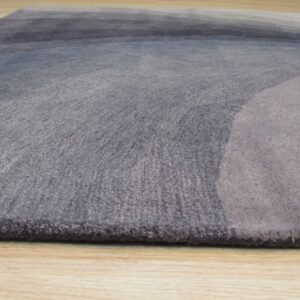 Medium-pile rug with blue and gray abstract gradient pattern shown on light wood flooring.