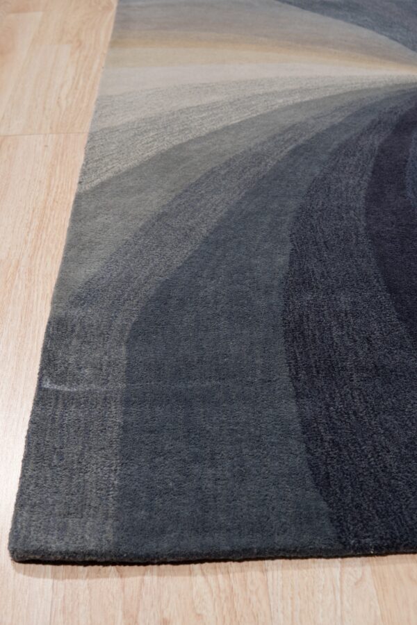 Abstract rug featuring gradient curved bands of dark blue, gray, and light beige on wood flooring.