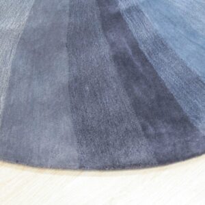 Plush circular rug detail showing radial blue and gray gradient bands on light wood floor.