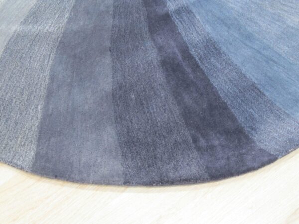 Plush circular rug detail showing radial blue and gray gradient bands on light wood floor.