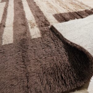 High-pile brown and beige geometric rug with a folded corner, revealing the woven backing on wood floor.
