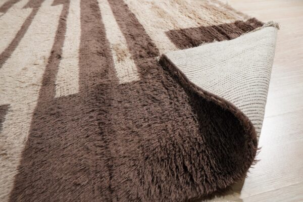High-pile brown and beige geometric rug with a folded corner, revealing the woven backing on wood floor.