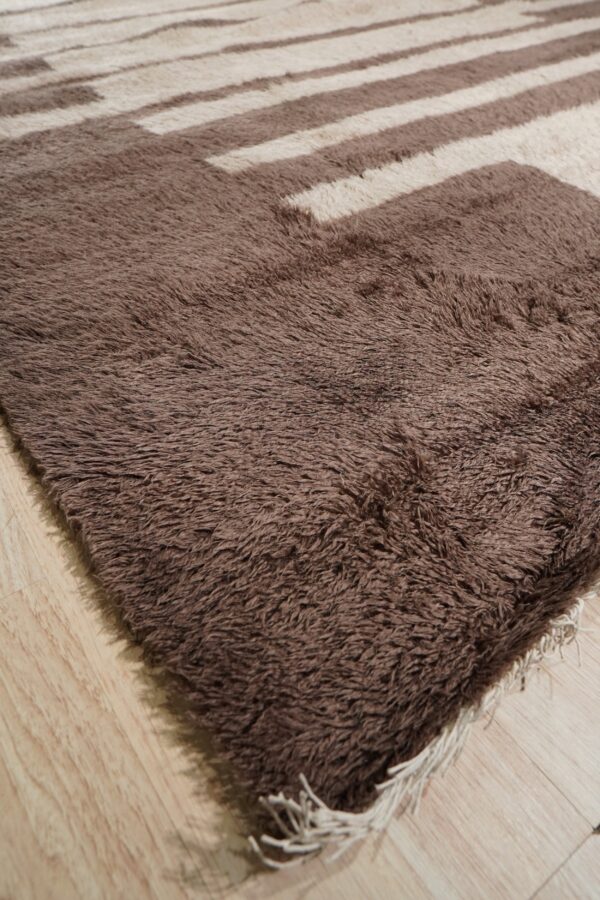 Shaggy brown and cream rug with a geometric striped pattern lies on light wood flooring.
