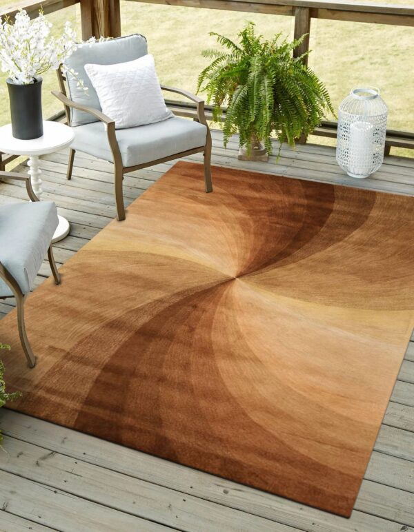 A brown and tan swirl-patterned rug sits on a gray wooden deck with patio chairs and plants.