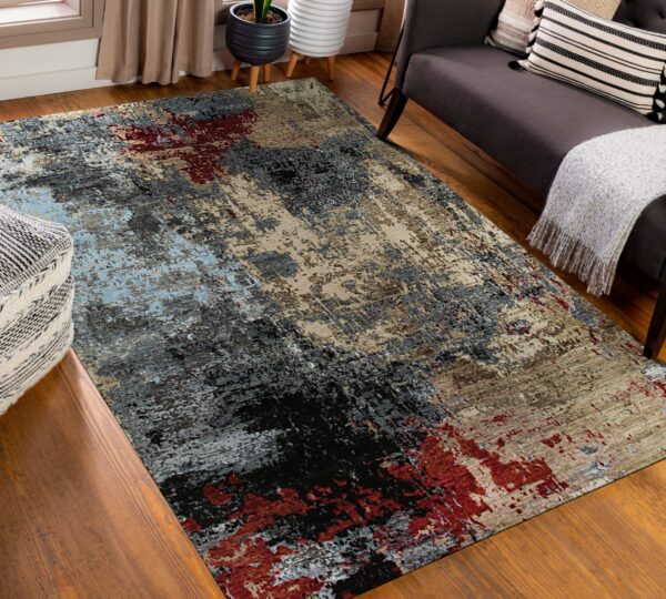 Abstract rug in gray, black, beige, red, and light blue rests on a wood floor beside a dark sofa.