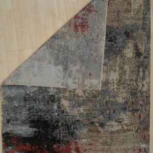 Abstract low-pile rug in tan, charcoal, gray, and red, displayed folded on light plank flooring.
