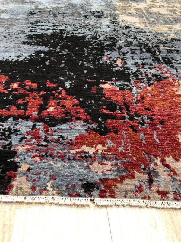 Abstract rug featuring red, black, and blue-gray distressed patches on a light wood floor.