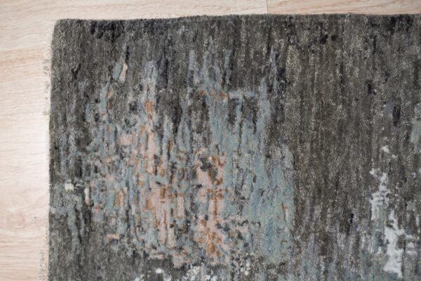 Textured gray rug with an abstract design in blue and beige shown on light wood flooring.