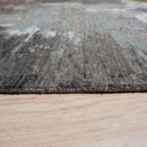 Low angle detail of a medium pile abstract rug in gray and blue resting on light wood flooring.
