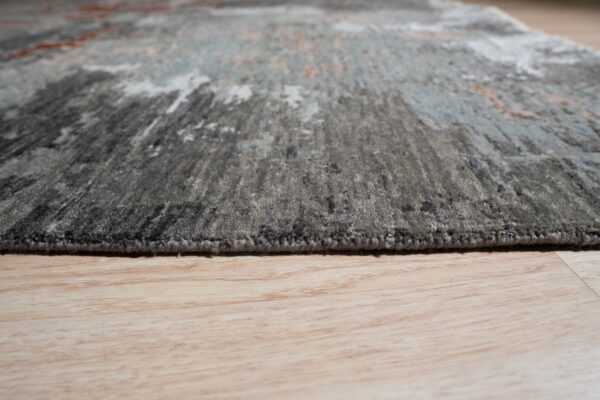 Low angle detail of a medium pile abstract rug in gray and blue resting on light wood flooring.