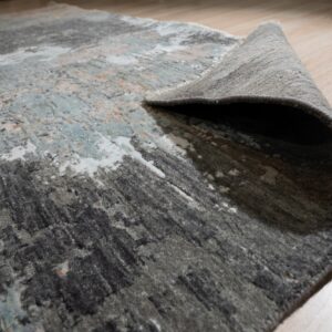High-low pile abstract rug in gray, teal, and white rolled up on light wood flooring.