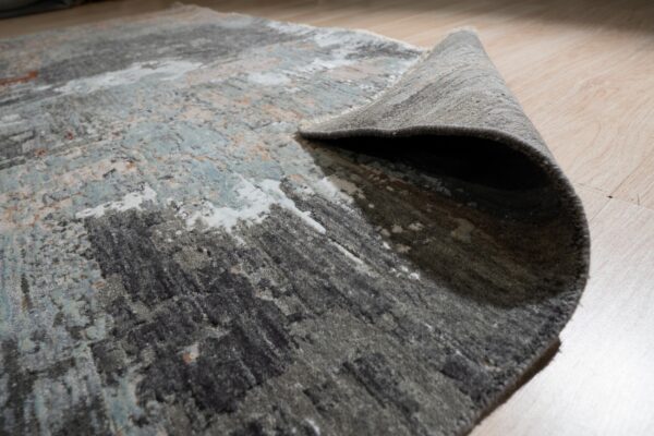High-low pile abstract rug in gray, teal, and white rolled up on light wood flooring.