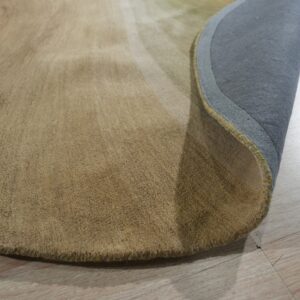 Curved tan medium-pile rug rolled back on light wood flooring, showing the gray backing fabric.