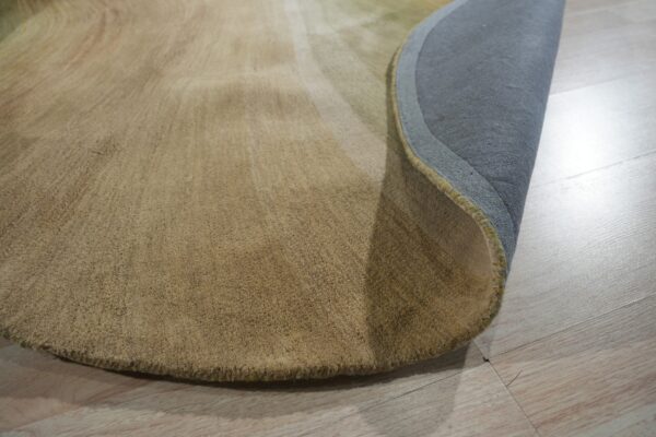 Curved tan medium-pile rug rolled back on light wood flooring, showing the gray backing fabric.