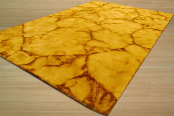 A golden yellow plush rug with a brown abstract cracked pattern rests on light wood plank flooring.