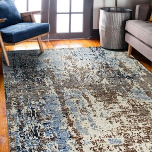 Abstract rug in blue, brown, black, and cream placed on wood flooring near a blue chair and gray sofa.