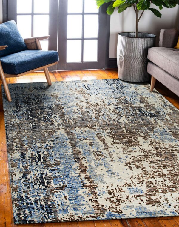 Abstract rug in blue, brown, black, and cream placed on wood flooring near a blue chair and gray sofa.