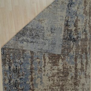 Beige, blue, and brown abstract rug with a pixelated pattern lies on light wooden floorboards.