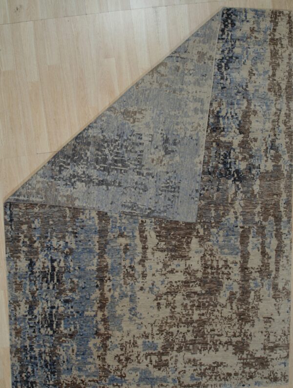 Beige, blue, and brown abstract rug with a pixelated pattern lies on light wooden floorboards.