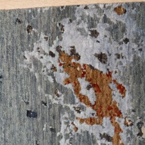 Close-up of a blue and rust abstract textured rug detail, featuring contrasting pile heights on light wood.