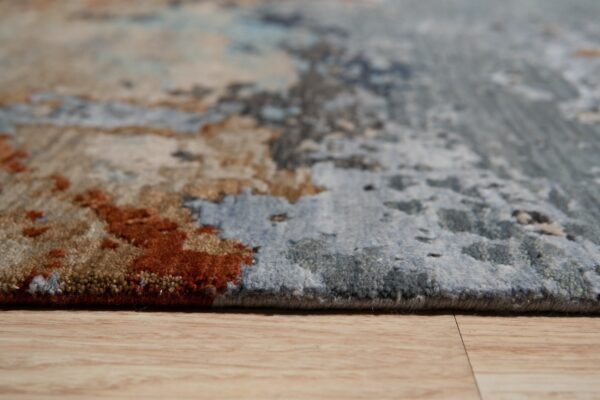 Close view of a multi-colored abstract rug edge showing tan, rust, and blue pile on light wood flooring.