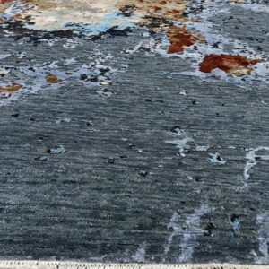 Highly textured gray rug with abstract rust and blue patches sits on light wood flooring.