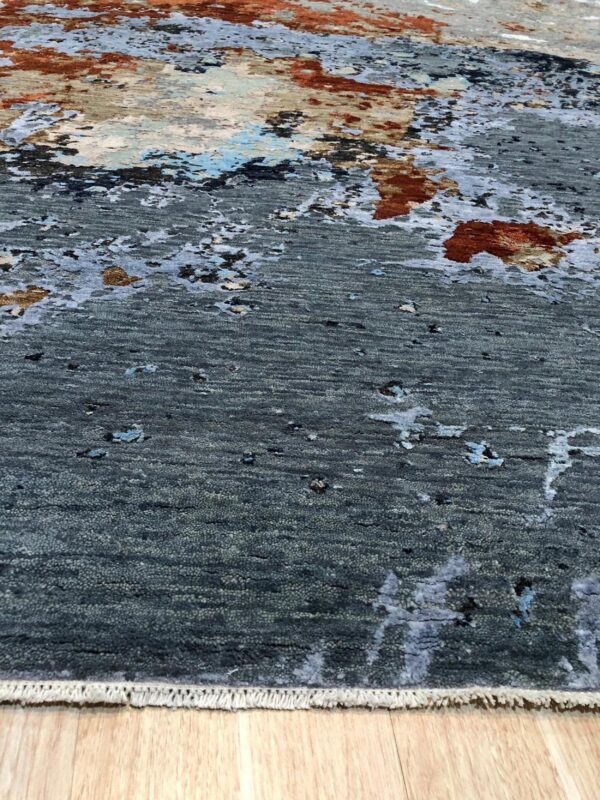 Highly textured gray rug with abstract rust and blue patches sits on light wood flooring.