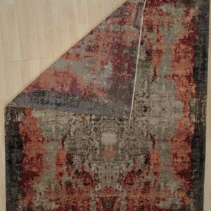 Abstract rug in earth tones, rust, and deep red on light wood flooring, with one corner folded back.
