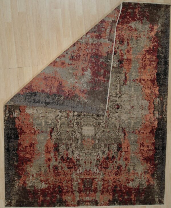 Abstract rug in earth tones, rust, and deep red on light wood flooring, with one corner folded back.