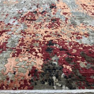 Abstract high-low pile rug in gray, burgundy, and peach tones sits on light wood flooring.