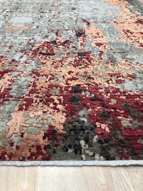 Abstract high-low pile rug in gray, burgundy, and peach tones sits on light wood flooring.