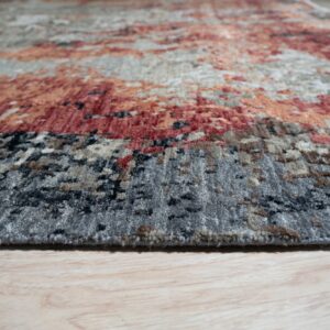Textured rug in abstract gray, rust, and cream patterns rests on light wood-look flooring.
