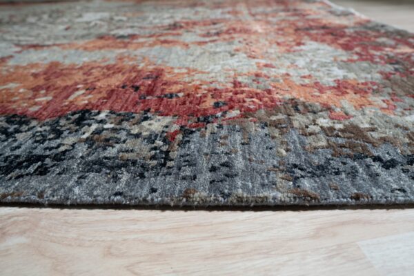Textured rug in abstract gray, rust, and cream patterns rests on light wood-look flooring.