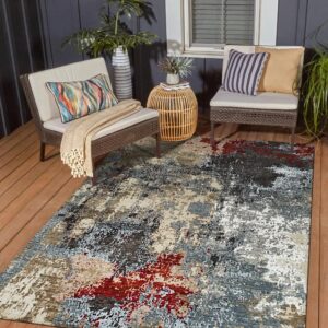 Abstract gray, red, and beige rug on a wood deck between two woven brown outdoor patio chairs.