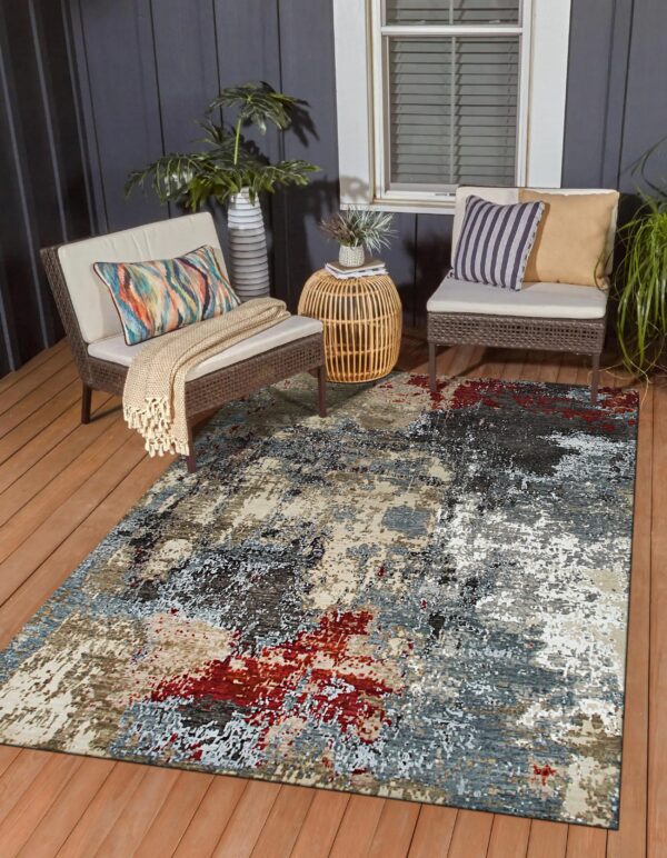 Abstract gray, red, and beige rug on a wood deck between two woven brown outdoor patio chairs.