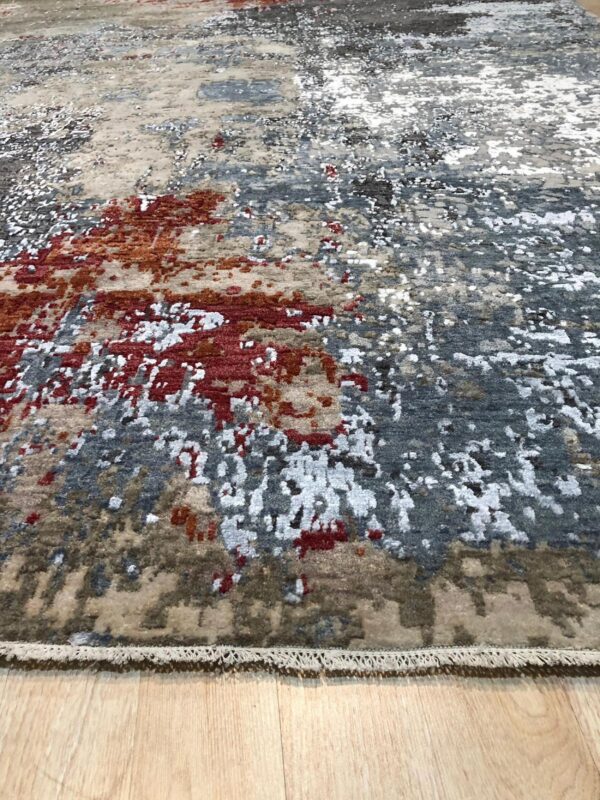 Textured abstract rug in tones of beige, gray, rust, and white on a light wood plank floor.