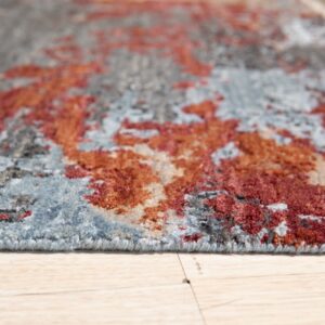 Abstract rug with medium pile in shades of gray, rust, and blue sits on light wood planks.