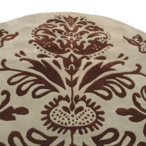 Light beige round rug detail featuring a carved dark brown scrolling floral and damask pattern.