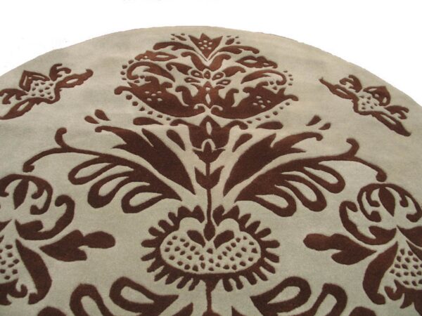 Light beige round rug detail featuring a carved dark brown scrolling floral and damask pattern.